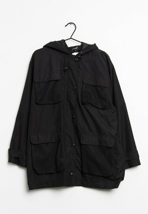 Veste noire à capuche avec quatre grandes poches avant à détails en mesh, fermeture par boutons et poignets ajustables, suspendue sur un cintre noir.