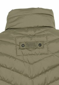 Helle olivgrüne Pufferjacke mit hohem Kragen und Zickzack-Steppmuster. Sie verfügt über ein Markenzeichen und zwei schwarze Metall-Druckknöpfe auf der Rückseite.