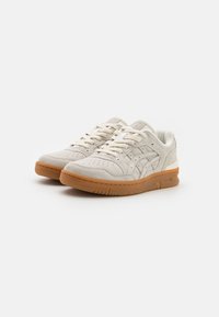 Sneakers in suede beige con dettagli perforati, lacci piatti e suola in gomma naturale. Presentano un accento bianco sul tallone e un design classico.