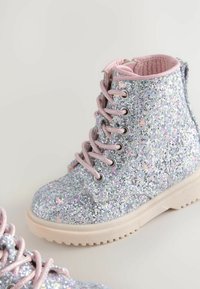 Bottines argentées pailletées avec des lacets et une doublure roses, présentant une semelle en caoutchouc et un dessus texturé et étincelant.