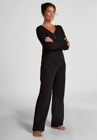 Zwarte top met lange mouwen, een V-hals en knoopdetails, gecombineerd met bijpassende zwarte broek met wijde pijpen. Zacht materiaal, comfortabele pasvorm, minimale structuur.