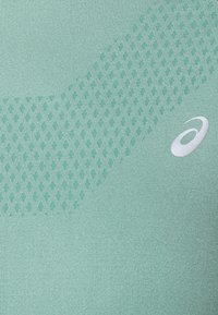 Tessuto atletico di colore verde chiaro con un motivo testurizzato a piccoli punti e una sezione liscia, dotato di un logo bianco.
