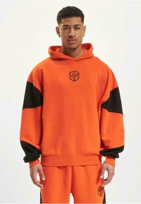 Oransje hettegenser med svarte detaljer, med et frontlogo og ribbede mansjetter. Laget av mykt stoff, med en avslappet passform og geometriske sømmer.