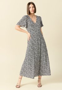 Mörkblå blommig maxikjol med V-ringning och fladderärmar, med en flödande silhuett och små vita blommönster. Silverfärgade sandaler med remmar.