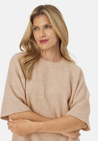 Beige striktrøje med korte ærmer og ribbet tekstur. Har en klassisk rund halsudskæring og subtile sprøjt i hele stoffet.