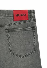 Grå denim jeans med en rød rektangulær label, der har "HUGO" i sort skrift på taljen, med en standard baglomme design.