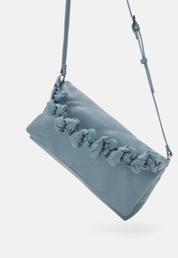 Borsa in pelle azzurro chiaro con dettaglio a trama intrecciata e cuciture diagonali. Presenta una tracolla regolabile e una forma rettangolare elegante.