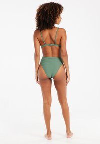 Žalias bikini komplektas su grioveliais. Viršus pasižymi reguliuojamais petnešomis ir užsegimu su kabliu. Aukštos juosmens kelnaitės su lygiu paviršiumi.