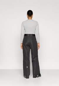 Sorte skibukser med en afslappet pasform, der har en robust talje, sidelås og logodetalje nær bunden. Glat, vandafvisende materiale.