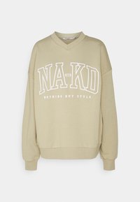 Sudadera de color beige claro con escote en forma de V y hombros caídos. Presenta texto impreso en blanco "NA-KD" y "NADA MÁS QUE ESTILO" en la parte delantera. Textura suave.