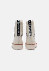 Botas de tobillo gris claro con un acabado texturizado, que cuentan con una correa de logo en blanco y negro en la parte trasera y una suela gruesa blanca.