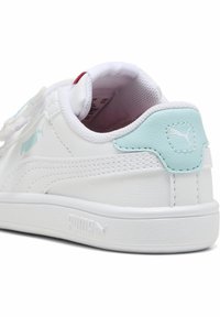Hvit lær sneaker med en glatt tekstur, med en lys blå aksent på hælen og en liten logo. Flat gummisåle og stikt detaljer.