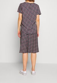 Blommig klänning i mörkt tyg med röda och vita mönster. Korta ärmar, knälång kjol och detaljer med knappar i ryggen. Bärs med vita sneakers.