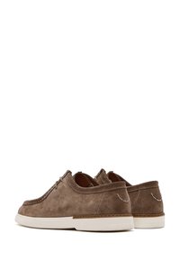 Scarpe in camoscio marrone con profilo basso, design con lacci, suola in gomma bianca, cuciture a contrasto e accenti decorativi minimalisti.