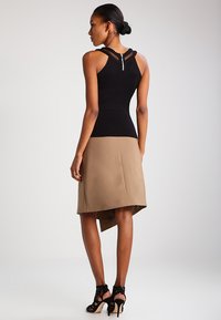 Haut sans manches noir avec des bretelles superposées et une fermeture éclair au dos, associé à une jupe beige à ourlet asymétrique ; tissu texturé et design ajusté.