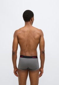 Gray men's boxer shorts with a black waistband featuring red "HUGO" branding, viewed from the back, showcasing a fitted design and smooth texture.