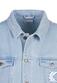 Light blue denim jacket with a spread collar, two chest pockets, brass buttons, and embroidered logo detail on the left pocket.