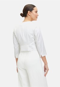 Valkoinen lyhyt takki, jossa on kolmannespuoliset hihat, sileä tekstuuri, kevyt peplum vyötäröllä ja sivurei'ät.