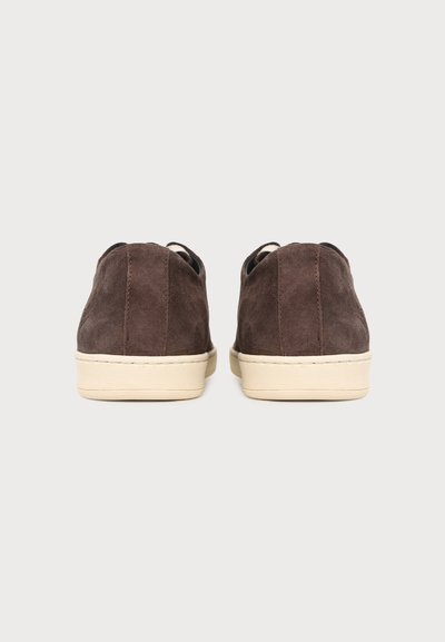 Paire de baskets en suède marron avec semelles en caoutchouc beige, vues de dos sur un fond clair uni.