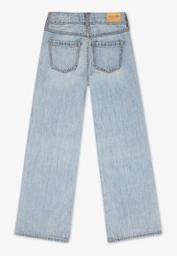 Jeans de denim lățiți, de culoare albastru deschis, văzuți din spate, cu două buzunare la spate și o etichetă de marcă bej pe talie.