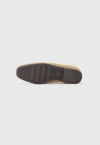 Schuhsohle aus strukturiertem braunem Gummi mit Rillen für besseren Halt, verbunden mit einem beigen Wildleder-Obermaterial, glattes und leicht geschwungenes Design.