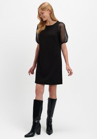 Czarna sukienka z krótkim rękawem i przezroczystymi bufkami, prosty krój i miękka tkanina. W zestawieniu z czarnymi botkami do kolan, minimalistyczny design.