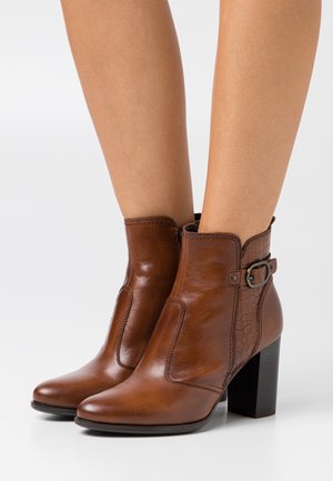 Bottines en cuir marron avec une finition lisse, un panneau latéral texturé, une boucle décorative et un talon carré.