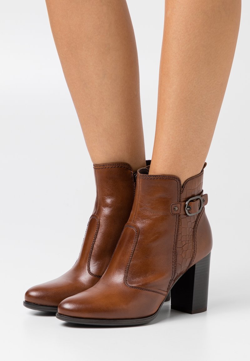 Brown leather ankle boots with a smooth finish, a textured side panel, a decorative buckle, and a square heel.