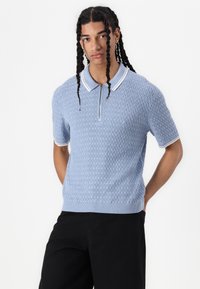 Light blue short-sleeve knitted polo shirt with textured pattern and white collar trim, featuring a half-zip design and ribbed hem.
