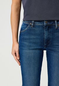 Jeans de mezclilla azul con forma ajustada, cinco bolsillos y un sutil desgastado. Presentan botones metálicos y una cintura con presillas estándar.