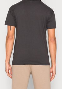 T-shirt di cotone nero con maniche corte e scollatura a girocollo; texture liscia; presenta cuciture minime all'orlo e alle maniche.