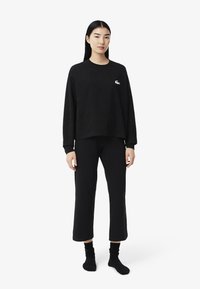 Sweatshirt preto com gola redonda e logótipo bordado, combinado com calças curtas pretas. Ambas as peças são feitas de um tecido macio e confortável.
