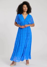 Blå maxiklänning med V-ringning, genomskinliga fladdermusärmar och dekorerade detaljer. Har en figurnära midja och en flödande kjol.