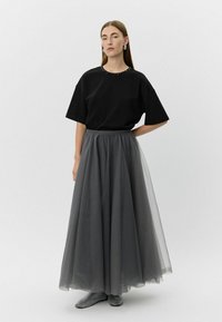 Must mustaga, millel on helmest kaelus, koos pikkade, voogavate hallide tüllseelikutega. Mudel kannab mustrilisi musti kingi.