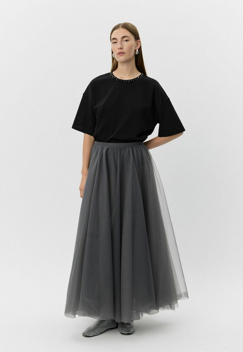 Must mustaga, millel on helmest kaelus, koos pikkade, voogavate hallide tüllseelikutega. Mudel kannab mustrilisi musti kingi.