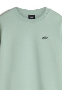 Sudadera verde claro con cuello redondo y puños acanalados, que presenta un pequeño logotipo negro de Vans en el lado izquierdo del pecho. Textura suave.