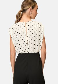 Black jumpsuit with a white polka dot blouse top. The blouse features a gathered design and a keyhole opening at the back.