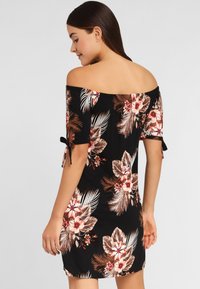 Vestido negro de flores, sin mangas y con mangas cortas, que presenta un patrón tropical en tonos beige y rosa, con detalles de lazo en los dobladillos de las mangas.
