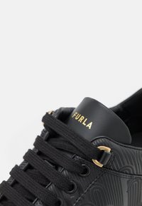 Baskets Furla noires avec motif texturé, lacets noirs, œillets dorés et nom de la marque en or sur la languette.