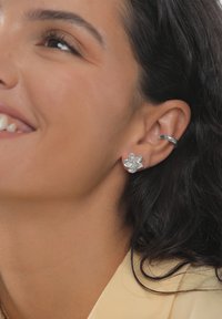 Strieborné náušnice v tvare kvetu s textúrovaným povrchom, zobrazené na modeli s tmavými vlasmi, ktorý má na sebe svetlý top.