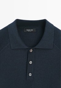 Polo blu navy con colletto a coste, abbottonatura a cinque bottoni e dettagli sulle spalle. Realizzata in morbido tessuto a maglia. Etichetta visibile all'interno.