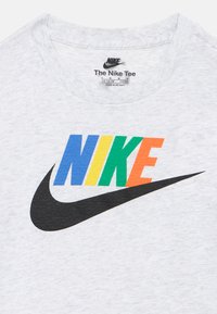T-shirt bianca Nike con testo "NIKE" multicolore in blu, giallo, verde e arancione sopra un grande logo swoosh nero.