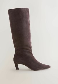Tmavo hnedá zamšová čižma po kolená s špicatou špičkou a nízkym, robustným podpätkom. Hladký povrch a bezšvový dizajn bez viditeľného kovania.