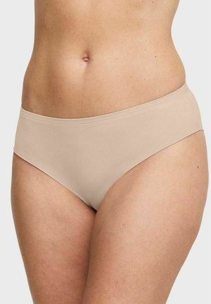 Beige naadloze hipsterdamesondergoed gedragen op de onderbuik en heupen van een vrouw tegen een lichte achtergrond.