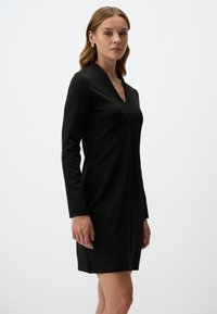 Robe noire à manches longues avec décolleté en V, coupe droite et texture lisse. Présente un subtil détail de couture et un design minimaliste.
