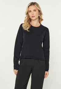 Pulover negru cu mâneci lungi, guler rotund și tiv ondulat. Fabricat dintr-un material moale și texturat, asortat cu pantaloni negri.