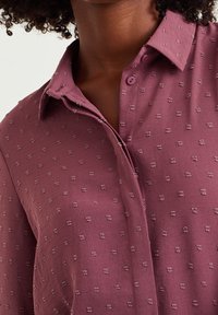 Mauve-pait, jossa on teksturoitu kuvio pienillä kohotetuilla pisteillä, kaulus ja klassinen nappisulku. Pehmeä kangas, jossa on rento istuvuus.