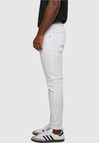 Biele slim-fit džínsy vyrobené z denimu, s päť vreckovým dizajnom, pútkami na opasok a kontrastným šitím, v kombinácii s bielymi a sivými teniskami.