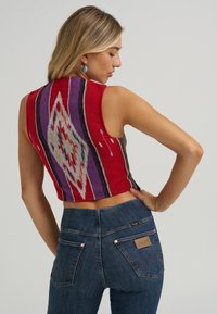 Gebreide cropped top in het rood met een geometrisch patroon in paars, groen en wit. Gecombineerd met donkerblauwe high-waisted jeans met zakdetails.