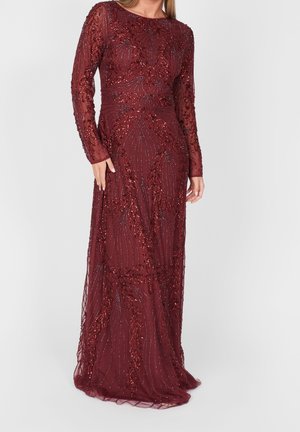 Vrouw draagt een bordeauxrode jurk met lange mouwen tot op de vloer, versierd met ingewikkelde pailletten- en kraaltjesdetails in bloemige en lineaire patronen.